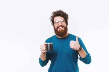 Neşeli adam portre sakal holfing fincan kahve ve başparmak göstermek yukarıya ile