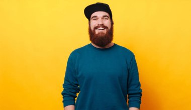 Sarı arka plan üzerinde poz şapkalı genç hipster adam portresi. Gülümseyen güneş gözlüğü, giyen adam vurdu studio sakallı.