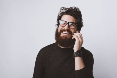 Gülümseyen ve beyaz arka plan telefonda konuşurken genç hayalperest adam. Dağınık saçlı sakallı adam.