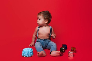 Studiou kırmızı arka plan üzerinde yıllar pastayla oturan çocukta mutlu bebek