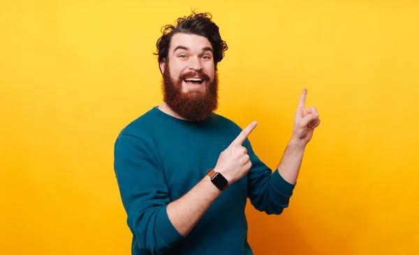 Portrait of cheerful bearded man pointing away over yellow background