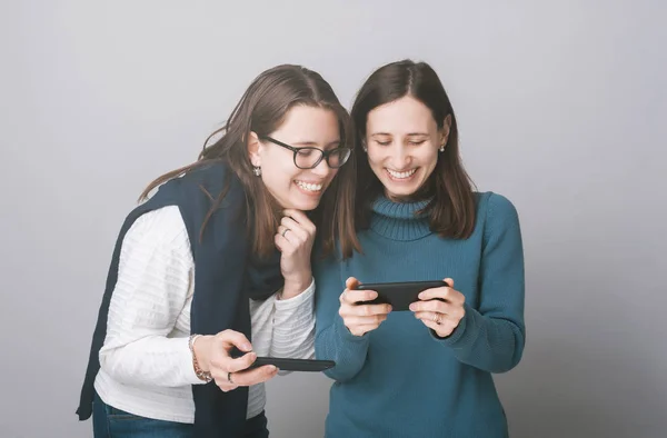 Duas Jovens Mulheres Sorridentes Olhando Para Smartphone Sobre Parede Cinza — Fotografia de Stock