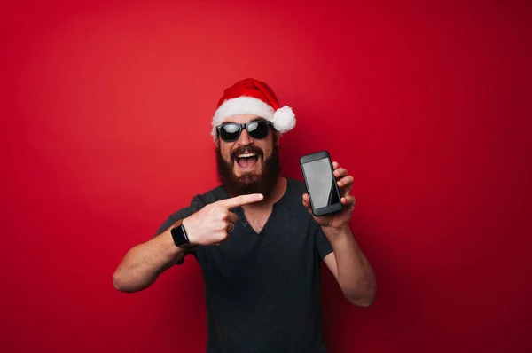 Fröhlicher Bärtiger Mann Mit Weihnachtsmannmütze Der Auf Das Smartphone Vor — Stockfoto