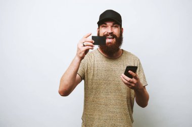 Neşeli adam sakallı fotoğrafı elinde onun smartphone ve yeni kart tutun