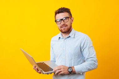 Neşeli bir genç adam tutun onun lapotop sarı arka plan üzerinde