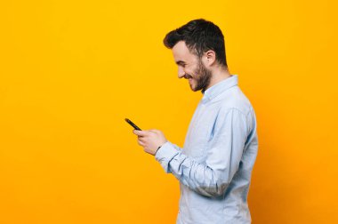 Genç gülümseyen ve sarı arka plan üzerinde smartphone kullanarak adam
