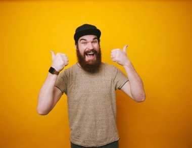 Şapka ve t-shirt, başparmak yukarıya ile giyen mutlu gülümseyen sakallı adam portresi