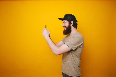 Sakallı adam şapka ve tshirt sarı arka plan üzerinde telefon kullanarak fotoğrafı