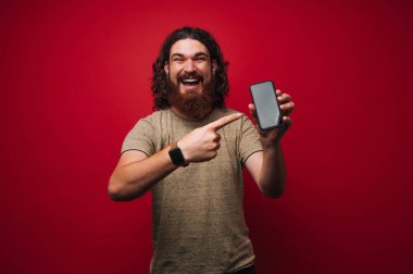 Sakal ve kıvırcık saç, mutlu neşeli adam cep telefonunu işaret
