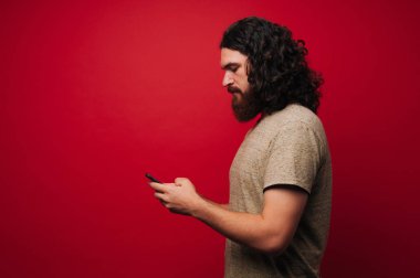 Uzun kıvırcık saç uisng bir telefon üzerinden kırmızı bir arka plan ile sakallı adam fotoğrafı