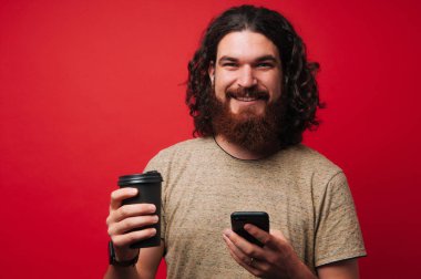 Kıvırcık saçlı kullanarak sakallı adam portresi telefon ve bir fincan çay ya da kahve tutun