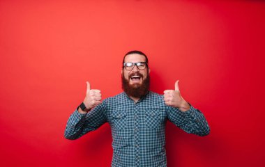 Sakal ve gözlük başparmak kırmızı arka plan üzerinde gösterilen mutlu smiiling adamla fotoğrafı