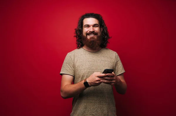 Smiliing bearded man with long hair, using phone and looking at camera