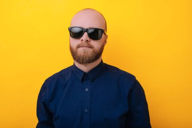 Tek sakallı yakışıklı genç ciddi ifade üzerinde sarı gbackground güneş gözlüğü takıyor ile portresi 