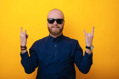 Bir rock yıldızı gibi. Kendine güvenen genç adam sarı arka plana karşı duran el hareketi güneş gözlüğü 