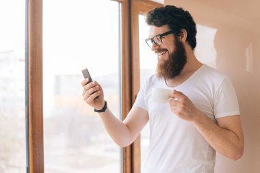 Mutfak yakışıklı adam gülümsüyor, sabahları kahve içme ve seyir akıllı telefon. 