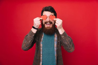 Kırmızı kalp gözünü tutarak mutlu sakallı adam. Sevgiliye arka plan. 