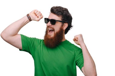 Rahat bir kıyafet giyen çok heyecanlı sakallı adam çığlık kadar yumruk yükselterek çok mutlu görünüyor