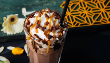 Soğuk kahve içecek frappe, çırpılmış krema ve karamel şurup, payet ve koyu gri masada kahve taneleri ile