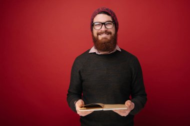 ders kitabı tutarak ve kameraya kırmızı arka plan üzerinde seyir bardaklarda sakallı adam 