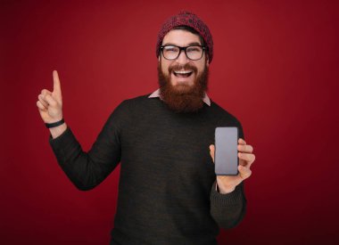 Kırmızı duvarın üzerinden Beyaz delikanlı göstermek onun smartphone, el ve parmak ile işaret çok mutlu