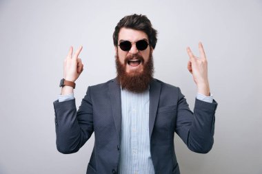 İşadamı Not ve rock'n roll işaret gösteren. İş kavramı, zengin insanlar ve başarı. Kapalı, stüdyo ışık gri arka plan üzerinde ateş 