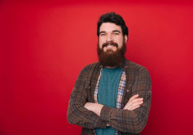 Sakallı yakışıklı emin çapraz kollar ve çeneme kaldırdı el ile gülümseme ile kameraya bakarak izole arka plan üzerinde. Pozitif düşünce.