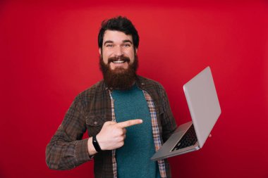 Bilgisayar dizüstü el ve parmak ile işaret çok mutlu kullanarak kırmızı duvar üzerinde adam genç sakallı 