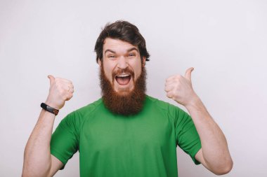 Evet beğendim. Başparmak kadar yükselterek ve geniş, olumlu geribildirim ayakta neşeli gri duvardan veren gülümseyen memnun ve tatmin yakışıklı erkek 