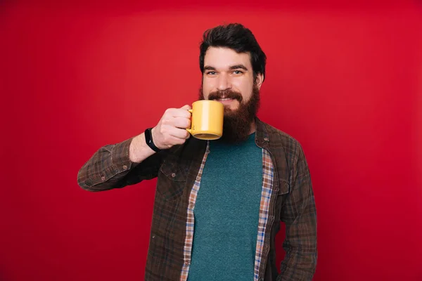 Bearded man with long beard and stylish hair on surprised face drink tea or coffee cup, morning and energy, refreshment