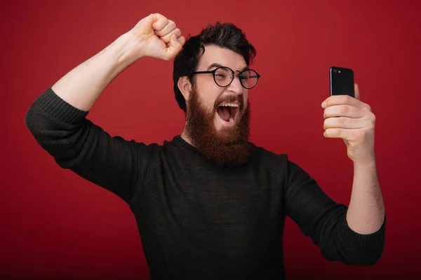 Homem Barbudo Positivo Óculos Apertando Punho Alegrando Enquanto Segurava Smartphone — Fotografia de Stock