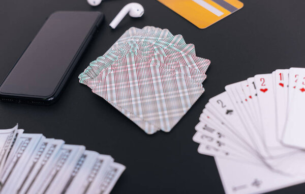 Selection of gambling items.  Playing cards and money, with a mobile phone, online gambling