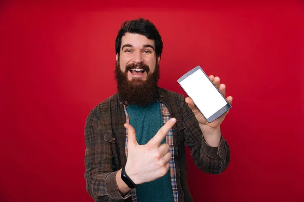 Retrato Jovem Barbudo Confiante Mostrando Telefone Celular Branco Apontando Dedo — Fotografia de Stock