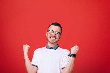 İzole kırmızı arka plan üzerinde başarı kutluyor memnun genç adam tshirt ve gözlük, portresi