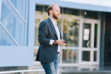Genç işadamı cam binanın önünde yürüyüş sakallı. Adam bloglama chetting.