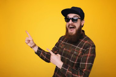 Sakallı adam uzakta iki parmağınızla sarı arka plan üzerinde izole kopya alanı işaret güneş gözlüğü heyecanlı