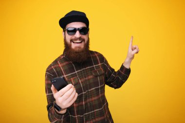 Genç adam manifatura smartphone el ve parmak ile tarafına işaret çok mutlu kullanarak bir ileti sakallı.