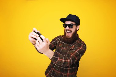 Smartphone üzerinde sarı arka plan üzerinde oynarken ekose gömlekli sakallı adam heyecanlı 