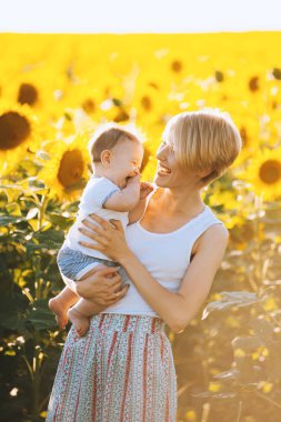 Gülümseyen ve küçük oğlunu çiçek açan ayçiçeği alanında tutarak oldukça genç anne