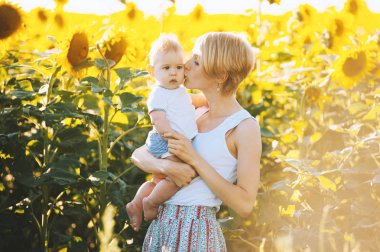 Güzel genç anne tutar ve ayçiçeği bir alanda bir bebek evlat öp