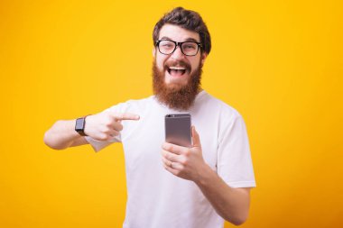 Promosyon kavramı. Smartphone vasıl işaret ve kameraya bakarak gülümseyen genç sakallı adam