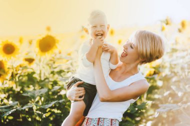 Neşeli Anne oğlunu sarılma. Genç anne ve küçük oğlu sarı ayçiçeği bir alana portre