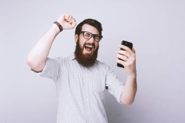 El hareketi yakışıklı heyecanlı bearde adam portresi silah ve bir akıllı telefon tutun 