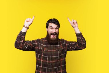 Genç berded adam sarı arka plan üzerinde kopya alanı iki eliyle işaret heyecanlı