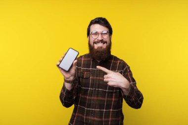 Mutlu gülümseyerek yuvarlak gözlüklü adam sakallı ve kareli gömlek cep işaret ediyor