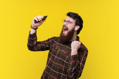 Yakışıklı sakallı hippi, heyecanlı müzik dinleme ve üzerine el hareketi arka plan sarı
