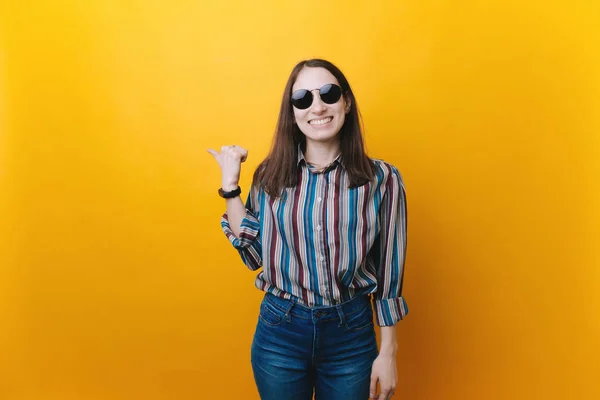 Young woman wearing sunglasses smiling broadly showing thumb up gesture, expression of like and approval