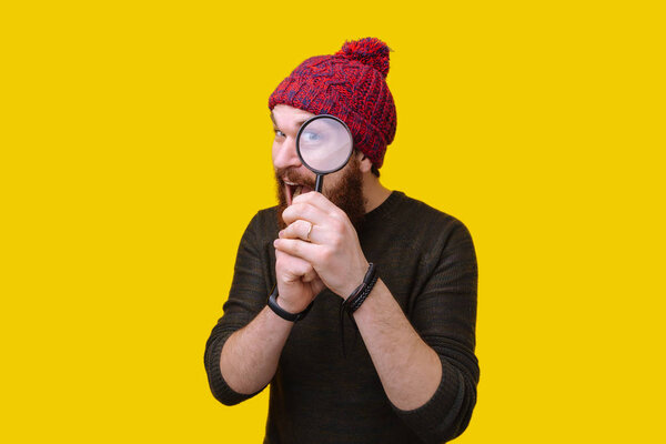 Handsome man with beard and red hat with magnifying glass, funny concept investigation