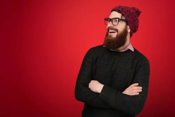 Smiling bearded man in sweater and red hat  which posing with crossed arms and looking away