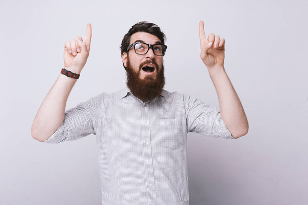 Portrait of cheerful  smart bearded man pointing up fingers at a copyspace
